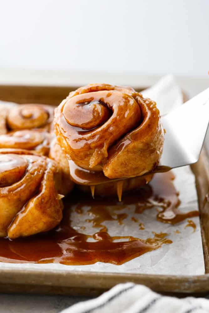 Caramel Rolls are as heavenly as they sound! Delicious and delicate cinnamon rolls are covered in caramel sauce that melts into every nook with absolutely divine flavor in every bite. I am not kidding when I say this is a next-level dessert experience! Caramel roll being lifted off parchment.