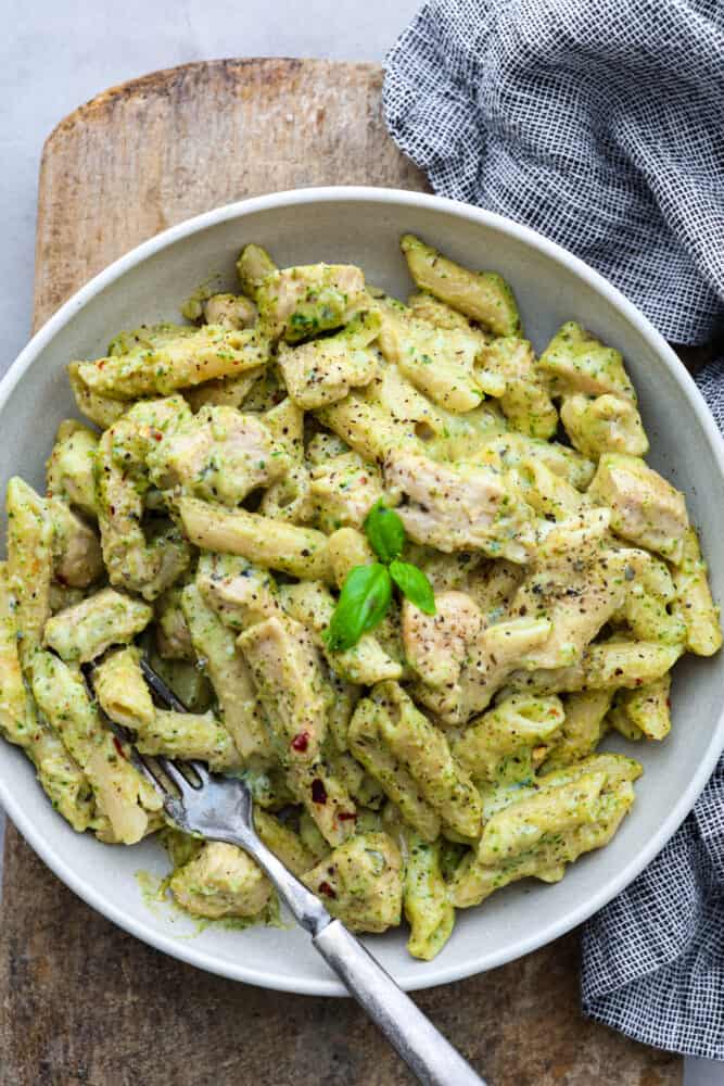 Chicken Pesto Pasta is made creamy with Parmesan, mozzarella, and heavy cream. Fresh basil pesto coats this pasta and chicken for the perfect pop of flavor in every bite. This is a quick and easy recipe that everyone will love! Chicken pesto pasta in a white bowl.