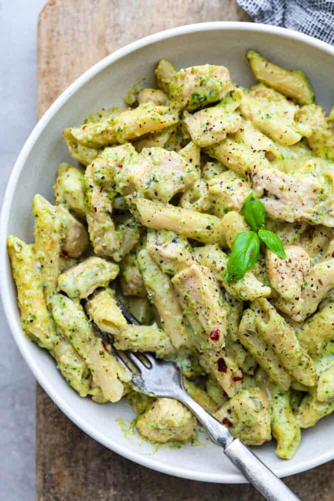 Chicken Pesto Pasta is made creamy with Parmesan, mozzarella, and heavy cream. Fresh basil pesto coats this pasta and chicken for the perfect pop of flavor in every bite. This is a quick and easy recipe that everyone will love! A close up on chicken pesto pasta in a white bowl.