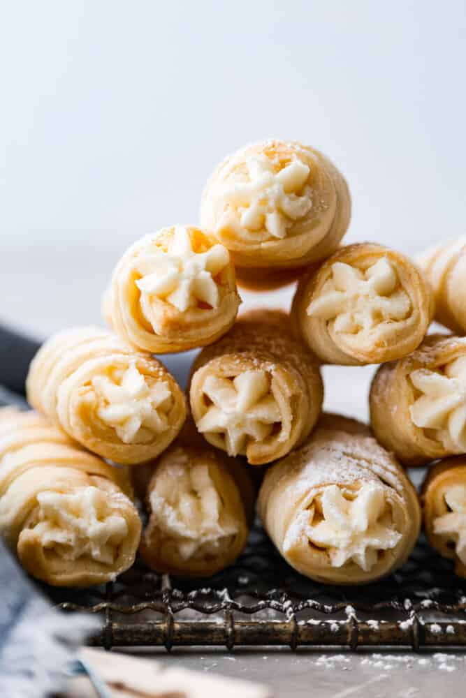 These clothespin cookies (also known as cream horns) are like little bites of heaven, filled with creamy goodness that'll make you forget all your problems - at least until you run out of them. They only take 30 minutes to prepare and are just the soft, creamy pastry you need in your life! Front view of cream horns stacked in a pyramid.
