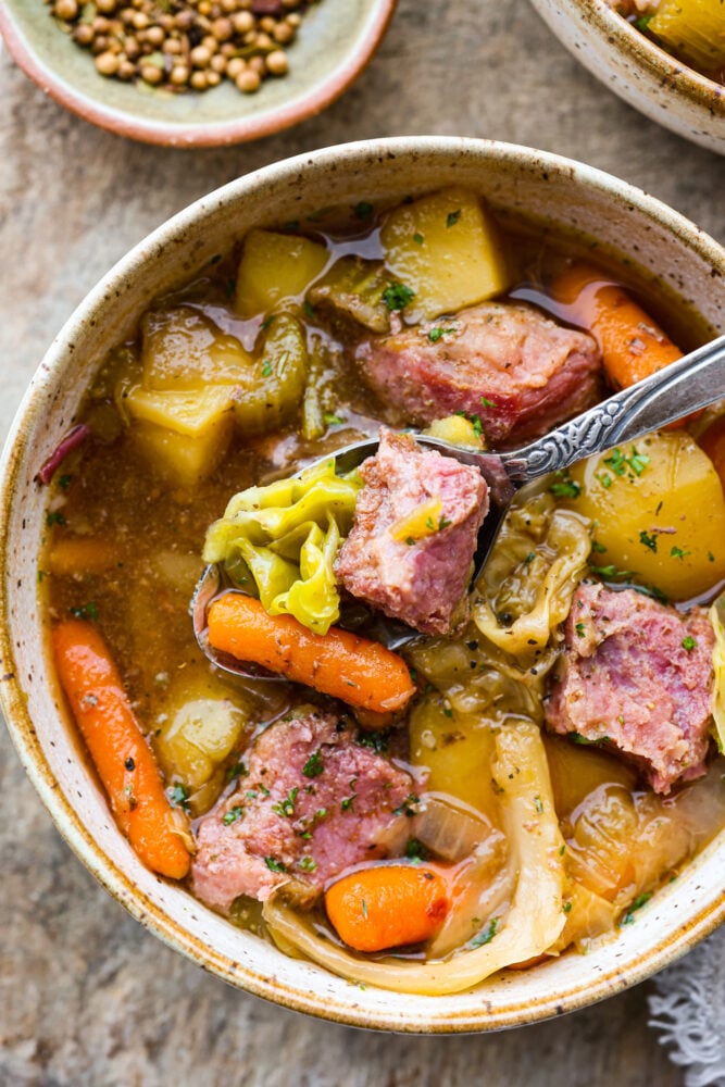 Corned Beef and Cabbage slow cook all day with hearty vegetables making one delicious stew! This is a classic recipe with nostalgic flavors, and it's so easy to whip up. A spoon taking a scoop out of the stew.