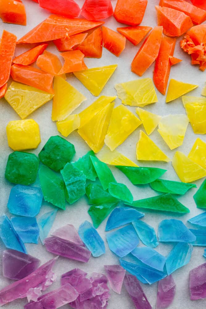 This gorgeous crystal candy tastes as good as it looks! Inspired by the Japanese candy "Kohakutou," it's such a fun treat to make with the kids. It has an addictive crunch to it and can be made with any flavor of your choosing! Closeup of orange, yellow, green, blue, and purple crystal candy.