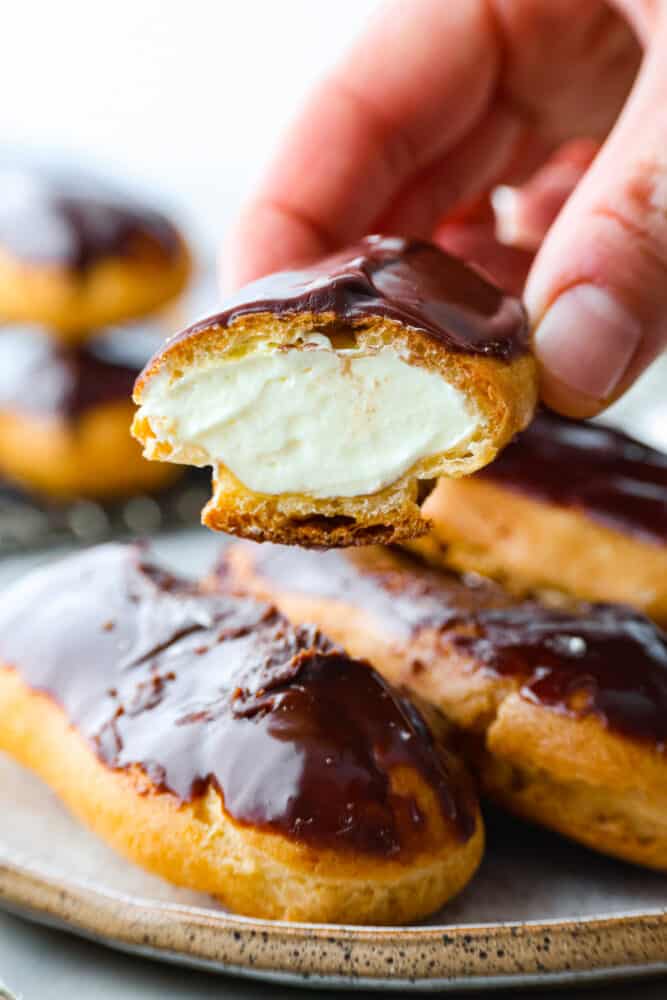 Skip the bakery and make your own delicious eclairs at home! These cream-filled delights are a labor of love and are sure to become one of your new favorite dessert recipes. Closeup of an eclair being picked up. The filling can be seen.