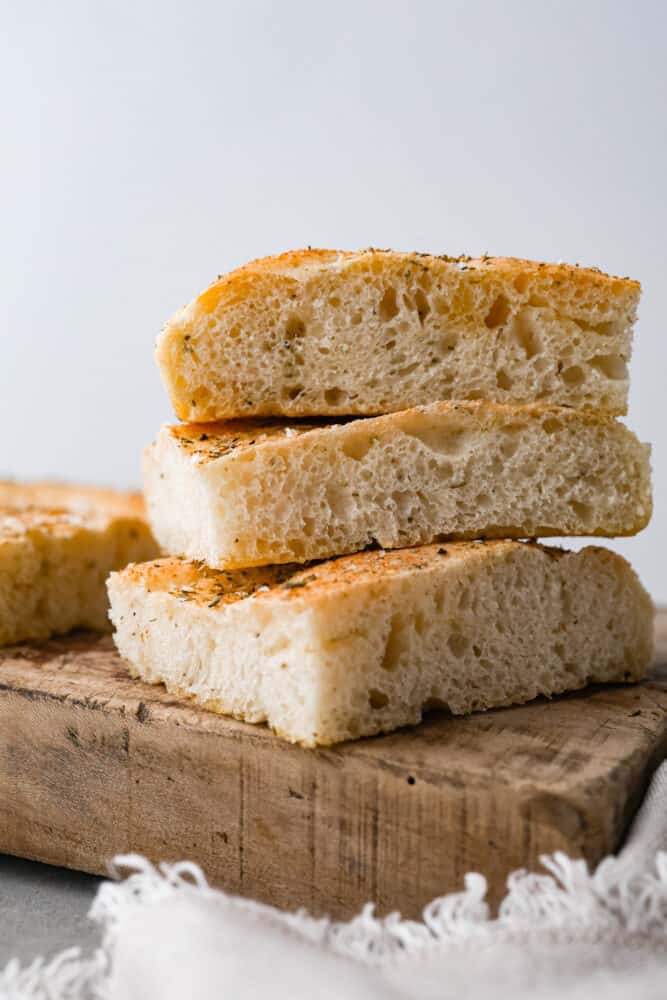 This Focaccia Bread recipe is easier than you think! Made with just a few ingredients and brushed with olive oil and Italian herbs, it's the perfect complement to any meal! Focaccia bread on a cutting board.