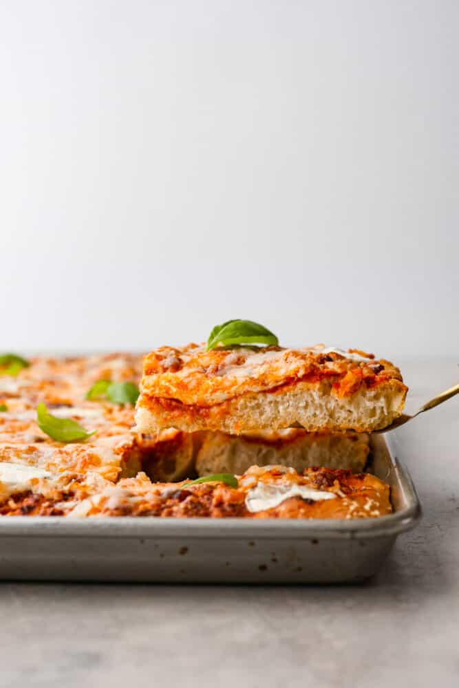 As if focaccia bread wasnโt good enough, now you can level it up with your favorite pizza toppings! Focaccia pizza is cheesy and flavorful, all on top of the most soft and dreamy crust! Serving a slice of focaccia pizza.