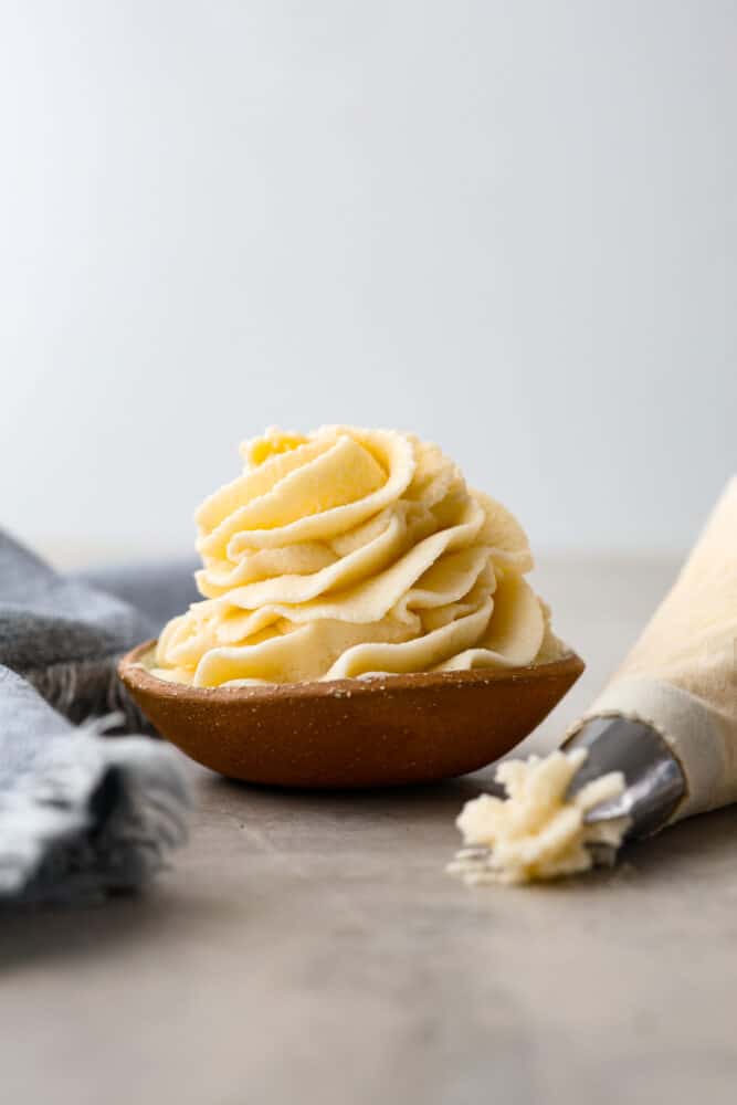 Ermine frosting, sometimes called roux frosting or flour frosting, is made by cooking flour, sugar, and milk. Never heard of it? I hadn't either, but it's actually a super light and fluffy frosting (that does NOT taste flour-y at all) that reminds me of sweet whipped cream. You are going to love this unique frosting! Ermine frosting in a little bowl with a piping bag next to it.