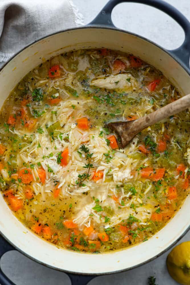 If you want a bright, light and filling dinner, then this lemon chicken orzo soup is for you! A savory and vibrant lemon chicken broth combined with orzo pasta is the perfect pair for a flavorful and delicious soup that is as satisfying as it is tasty. A look at the soup in a pot with a wooden spoon in it.