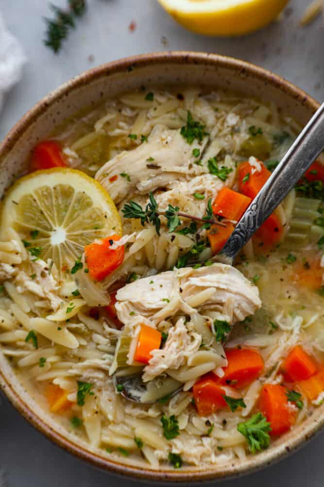 If you want a bright, light and filling dinner, then this lemon chicken orzo soup is for you! A savory and vibrant lemon chicken broth combined with orzo pasta is the perfect pair for a flavorful and delicious soup that is as satisfying as it is tasty. A close up on a bowl of lemon chicken orzo soup.