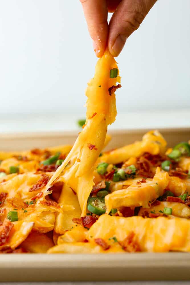 For your next cheat day, look no further than these loaded fries with all the fixin's: melty colby jack cheese, crispy bacon, tangy green onions, and a little kick of jalapenos! They're so good, you might just forget you're actually eating a vegetable (potatoes totally count, right?). A fry being picked up.