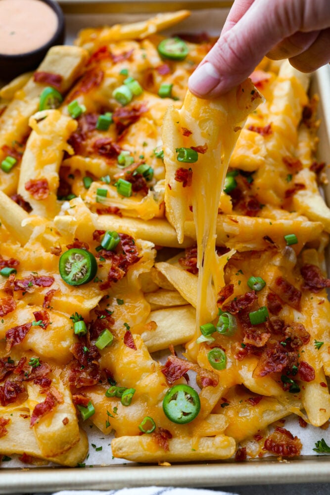 For your next cheat day, look no further than these loaded fries with all the fixin's: melty colby jack cheese, crispy bacon, tangy green onions, and a little kick of jalapenos! They're so good, you might just forget you're actually eating a vegetable (potatoes totally count, right?). Closeup of a cheese fry being pulled from the pan.