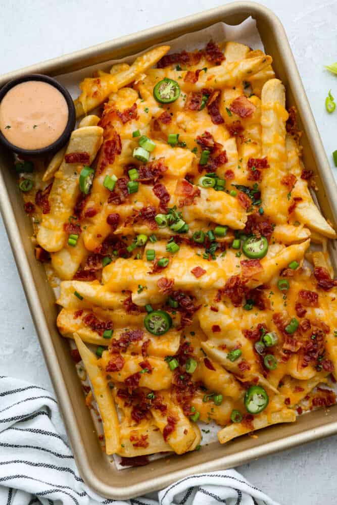 For your next cheat day, look no further than these loaded fries with all the fixin's: melty colby jack cheese, crispy bacon, tangy green onions, and a little kick of jalapenos! They're so good, you might just forget you're actually eating a vegetable (potatoes totally count, right?). Top-down view of loaded fries in a sheet pan.