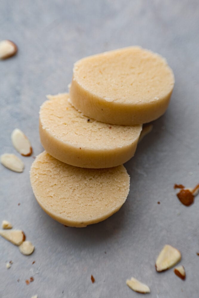 This Easy Homemade Marzipan will take your baking to the next level! It's a quick and simple recipe that will bring delicious almond flavor to your cakes and cookies. It's also easily colored and shaped into fun decorations! Sliced marzipan on a table.