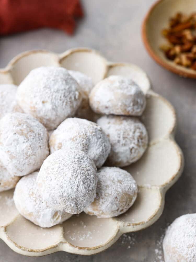 Mexican wedding cookies are buttery, nutty, and coated in powdered sugar that makes them oh-so-good. They are usually a celebratory dessert, but they are so yummy you will want them all the time! The cookies on a scalloped white plate.