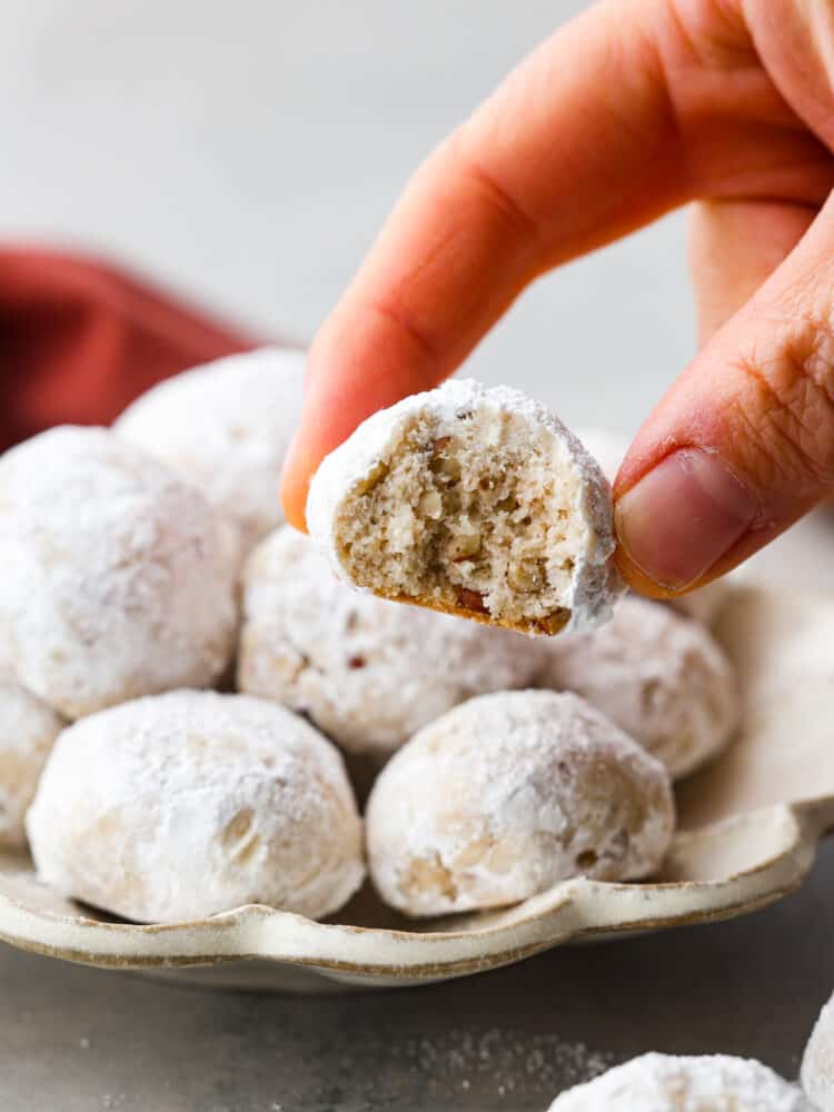 Mexican wedding cookies are buttery, nutty, and coated in powdered sugar that makes them oh-so-good. They are usually a celebratory dessert, but they are so yummy you will want them all the time! A hand holding a Mexican wedding cookie with a bite taken out of it.