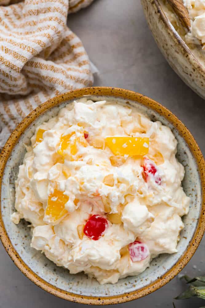 Get ready for this Pineapple Fluff to become your most requested recipe for potlucks! Similar to orange fluff, it's a delicious blend of pineapple chunks, coconut cream, marshmallows, and coconut flakes. It's seriously addicting and so easy to make! A close up of pineapple fluff in a bowl.