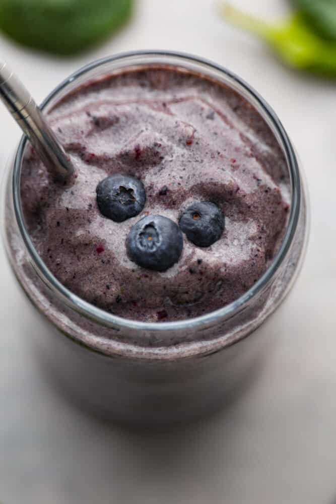 A protein smoothie is easy to digest and full of nutrients to keep your body happy until lunch. Not to mention it's absolutely delicious! Try out this recipe and you'll be hooked. A close up on a protein smoothie with fresh blueberries on top.