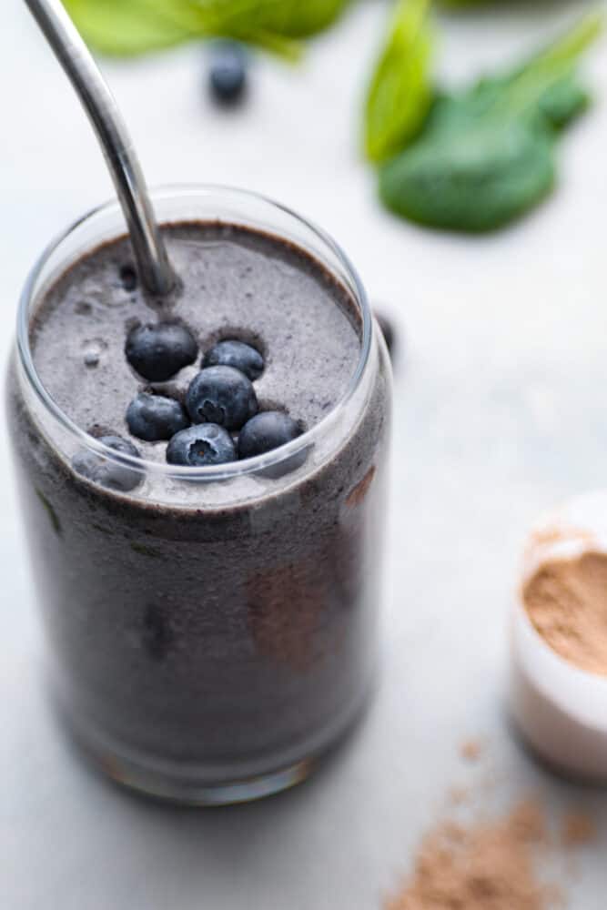 A protein smoothie is easy to digest and full of nutrients to keep your body happy until lunch. Not to mention it's absolutely delicious! Try out this recipe and you'll be hooked. A close up on a blueberry protein smoothie with a metal straw.