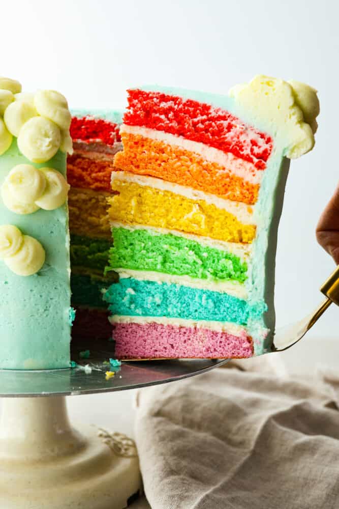 This gorgeous rainbow cake is the best way to add a splash of color to any special occasion! Not only is this cake beautiful to look at, but itโs extra moist and topped with luscious homemade buttercream. Itโs the perfect dessert for birthdays, Saint Patrickโs Day, and more! Serving a piece of rainbow cake with a cake spatula.