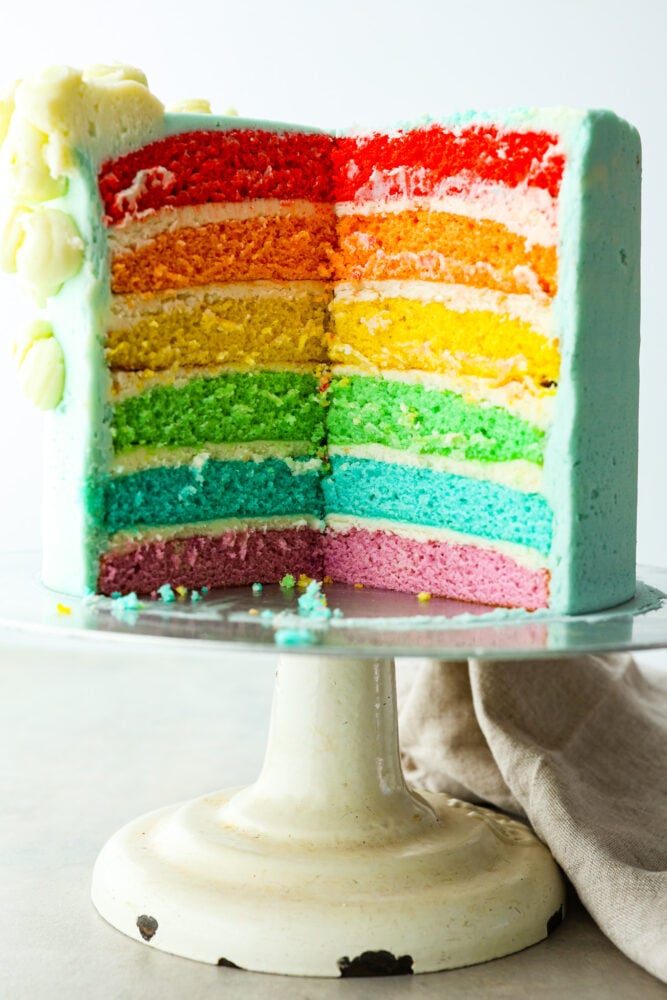 This gorgeous rainbow cake is the best way to add a splash of color to any special occasion! Not only is this cake beautiful to look at, but itโs extra moist and topped with luscious homemade buttercream. Itโs the perfect dessert for birthdays, Saint Patrickโs Day, and more! A whole rainbow cake with a slice cut out of it.