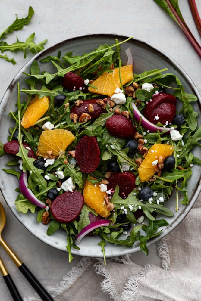 This roasted beet salad will have you singing the praises of this root veggie and begging for seconds! It's tossed with fruit, nuts, and crumbled cheese all coated in a delicious homemade balsamic vinaigrette. A light lunch that's both healthy and delicious! Top-down view of salad served in a gray stoneware bowl.