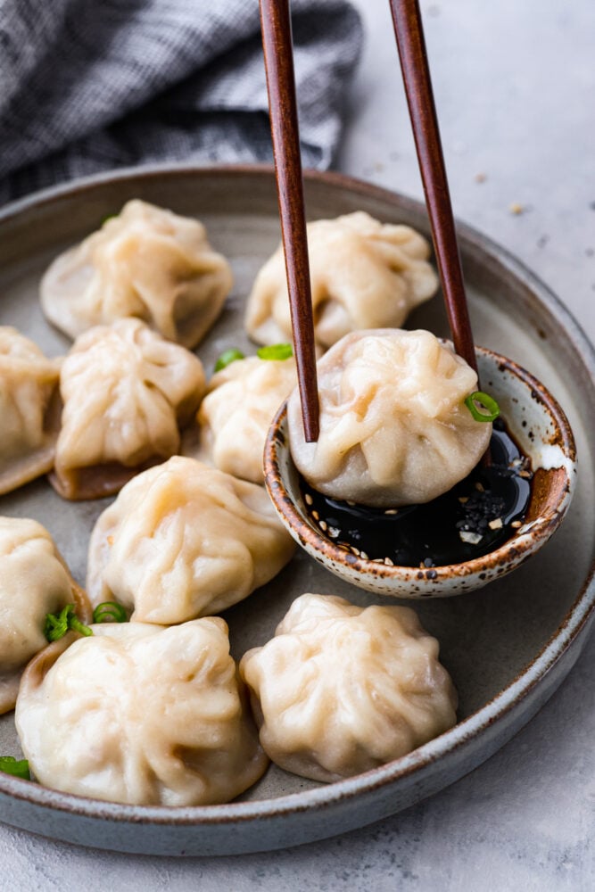 Chinese soup dumplings are delicious homemade wrappers filled with perfectly seasoned pork and soup. Yes, these dumplings are FILLED with soup! How do you get soup inside of a dumpling? It's like magic! This recipe is simple, delicious, and something everyone will enjoy. Soup dumplings being dipped in sauce with chop sticks.