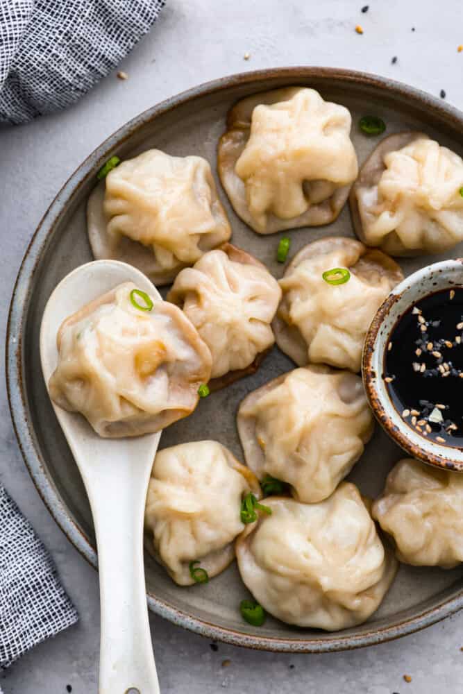 Chinese soup dumplings are delicious homemade wrappers filled with perfectly seasoned pork and soup. Yes, these dumplings are FILLED with soup! How do you get soup inside of a dumpling? It's like magic! This recipe is simple, delicious, and something everyone will enjoy. Soup dumplings on a plate with a spoon.