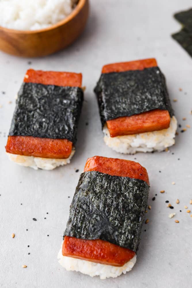 Spam musubi is a classic Hawaiian snack or on-the-go lunch, made with a slice of seared spam on top of rice, all wrapped in crispy seaweed! It has a delicious soy sauce glaze that makes each bite extra flavorful. Top-down view of 3 spam musubi.