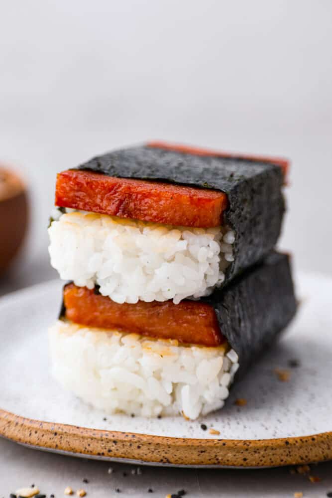 Spam musubi is a classic Hawaiian snack or on-the-go lunch, made with a slice of seared spam on top of rice, all wrapped in crispy seaweed! It has a delicious soy sauce glaze that makes each bite extra flavorful. 2 spam musubi stacked on top of each other.