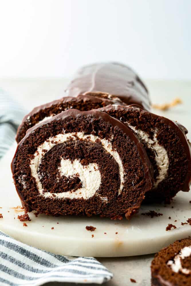 A classic and beautiful dessert, this Swiss Roll Cake is a rich chocolate sponge filled with pillowy whipped cream and covered in a chocolate ganache. This dessert is not only stunning, it's also incredibly tasty and every chocolate lover's dream! A slice of swiss roll cake on a plate.