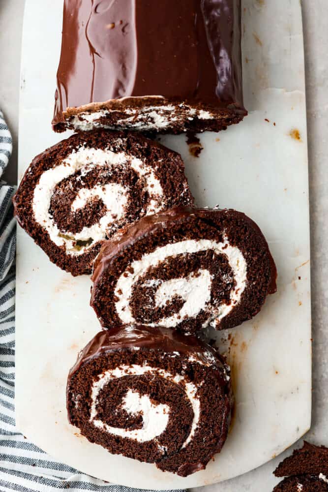 A classic and beautiful dessert, this Swiss Roll Cake is a rich chocolate sponge filled with pillowy whipped cream and covered in a chocolate ganache. This dessert is not only stunning, it's also incredibly tasty and every chocolate lover's dream! An overhead view of the swiss roll pieces on a cutting board.