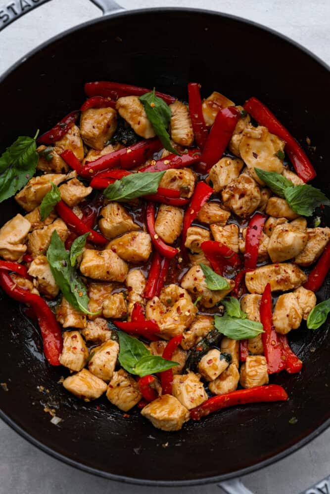 Thai Basil Chicken is a quick and easy chicken dinner that is bursting with fresh flavors. Bell peppers, fresh basil, and a unique blend of sauces make this chicken so crave-able! A look at the Thai basil chicken in the wok.