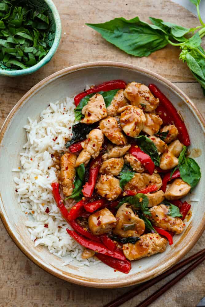 Thai Basil Chicken is a quick and easy chicken dinner that is bursting with fresh flavors. Bell peppers, fresh basil, and a unique blend of sauces make this chicken so crave-able! Thai basil chicken on a white plate.