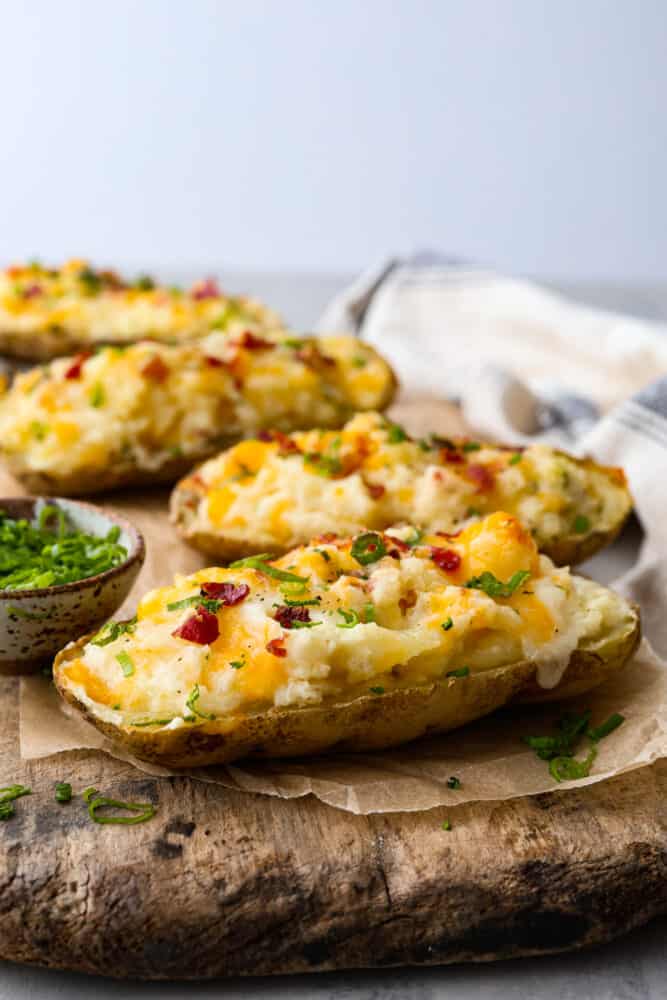What's better than a regular baked potato? A twice baked potato, of course! They are the ultimate comfort food - creamy, savory, and packed with cheesy goodness. Whether you're cooking for one or for a crowd, these spuds are easy to make and impossible to resist. Twice-baked potatoes topped with bacon, cheese, and green onions, served on a wooden board.