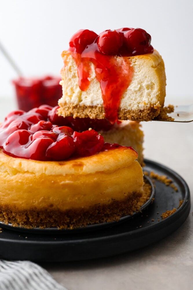 Get ready to indulge in the tastiest and easiest cheesecake you'll ever make! My air fryer never fails to impress- this amazing dessert is another great recipe to add to the list! When you're craving something sweet, air fryer cheesecake requires minimal effort and time, and is a great way to impress your guests or treat yourself to something special. Serving a slice of air fryer cheesecake topped with cherry pie filling.