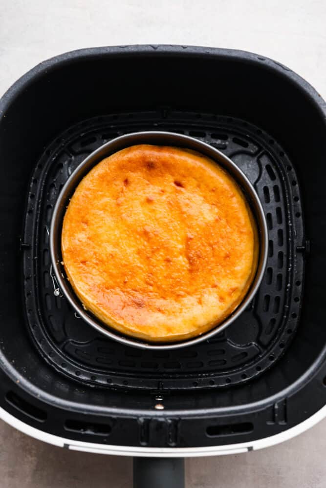 Get ready to indulge in the tastiest and easiest cheesecake you'll ever make! My air fryer never fails to impress- this amazing dessert is another great recipe to add to the list! When you're craving something sweet, air fryer cheesecake requires minimal effort and time, and is a great way to impress your guests or treat yourself to something special. A cooked cheesecake in the bottom of an air fryer basket.