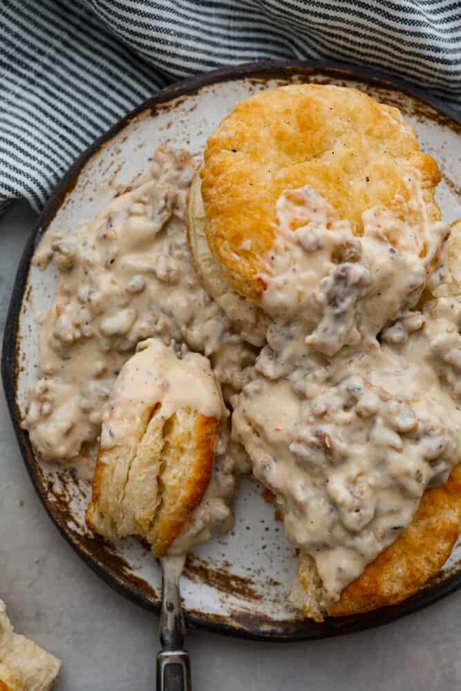 Biscuits and Gravy is the ultimate comfort food dish! Tender and flaky homemade biscuits are topped with creamy sausage gravy. This is such a simple recipe that is full of rich and nostalgic flavors, you've got to try it! An overhead view of the biscuits and gravy on a plate.