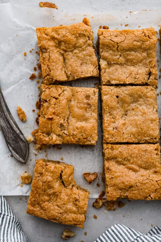 These chewy brown butter blondies are enhanced with the rich flavor of browned butter and loaded with (optional) nuts and candy pieces. Don't worry if you've never browned butter before, it's easy and I'll walk you through the steps below! An overhead view of brown butter blondies on parchment with one piece with a bite taken out of it.