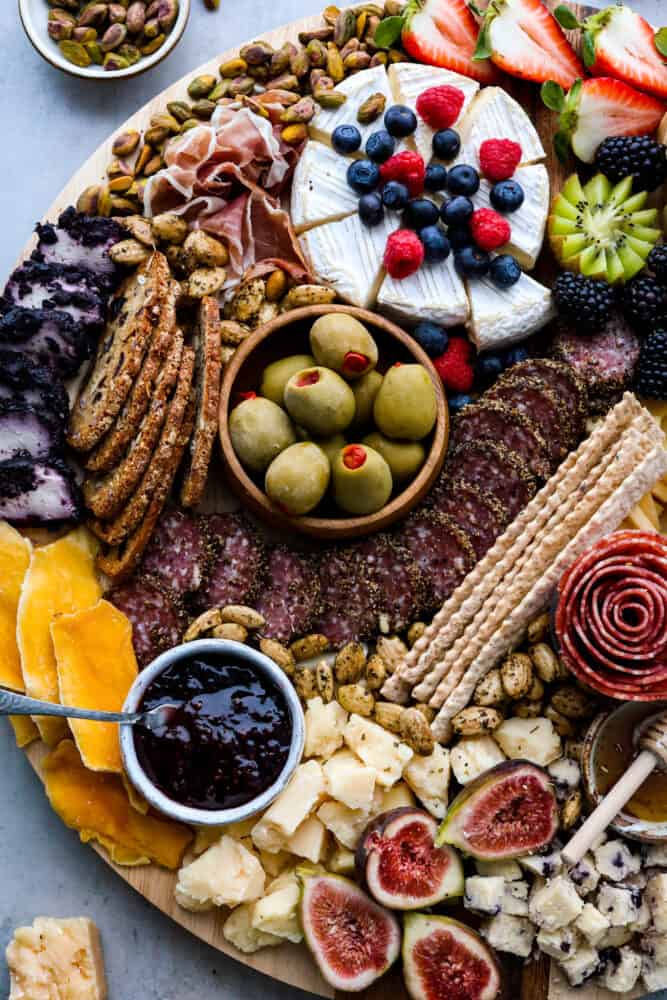 Charcuterie boards are the ultimate party trick that never fail to impress! These beautiful displays of meats, cheeses, fruits, and nuts are not only eye-catching but also incredibly delicious. Don't be intimidated by how Pinterest-worthy they look, because assembling one is a lot easier than you think. Here are all the ins and outs on how to make a charcuterie board at home! Closeup of various meats, cheeses, crackers, fruits, and spreads.