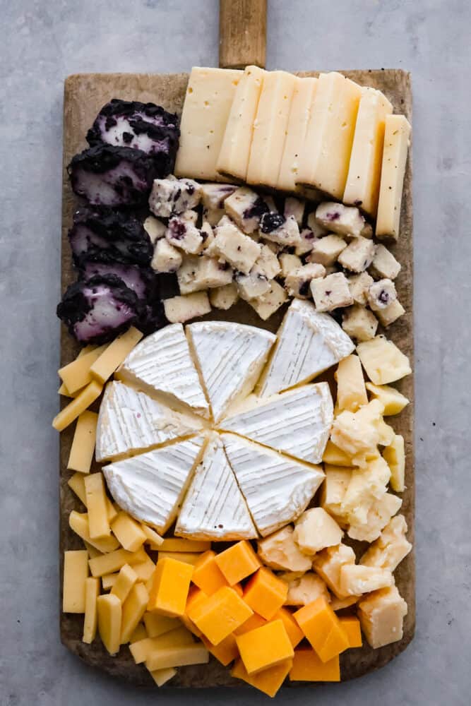 Charcuterie boards are the ultimate party trick that never fail to impress! These beautiful displays of meats, cheeses, fruits, and nuts are not only eye-catching but also incredibly delicious. Don't be intimidated by how Pinterest-worthy they look, because assembling one is a lot easier than you think. Here are all the ins and outs on how to make a charcuterie board at home! Top-down view of an assortment of cheeses on a wooden board.