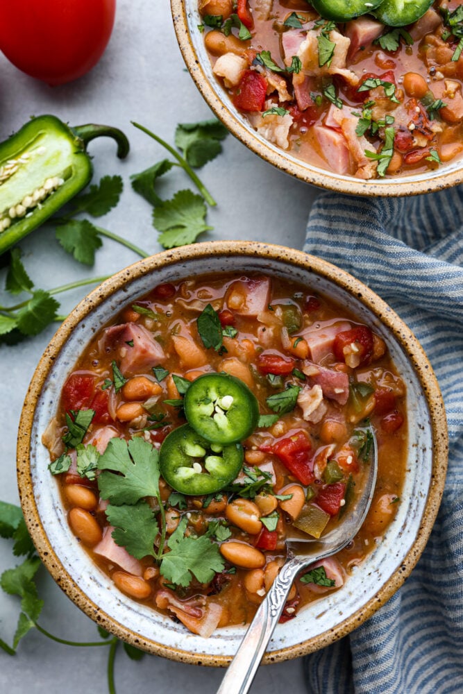 Mexican Charro Beans, also known as Frijoles Charros, are loaded to the brim with flavor! Pinto beans are cooked in a chicken broth seasoned with warm and inviting spices. Throw in some bacon, tomato, onions, ham, and jalapeños for the perfect blend of bold flavors. Charro beans in a bowl with a spoon.