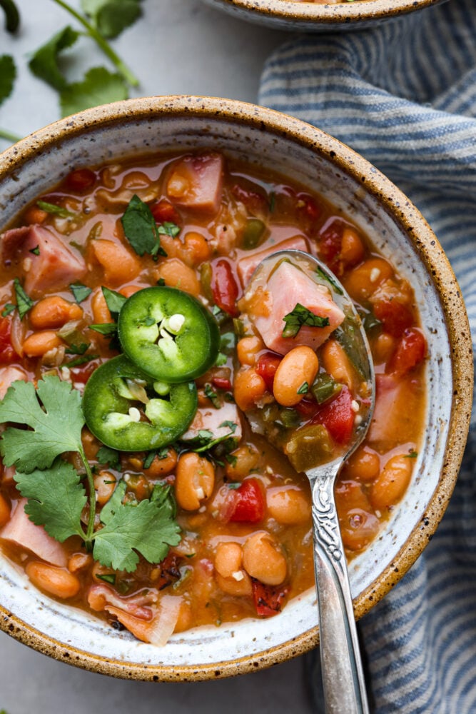 Mexican Charro Beans, also known as Frijoles Charros, are loaded to the brim with flavor! Pinto beans are cooked in a chicken broth seasoned with warm and inviting spices. Throw in some bacon, tomato, onions, ham, and jalapeños for the perfect blend of bold flavors. A close up of a bowl of charro beans.