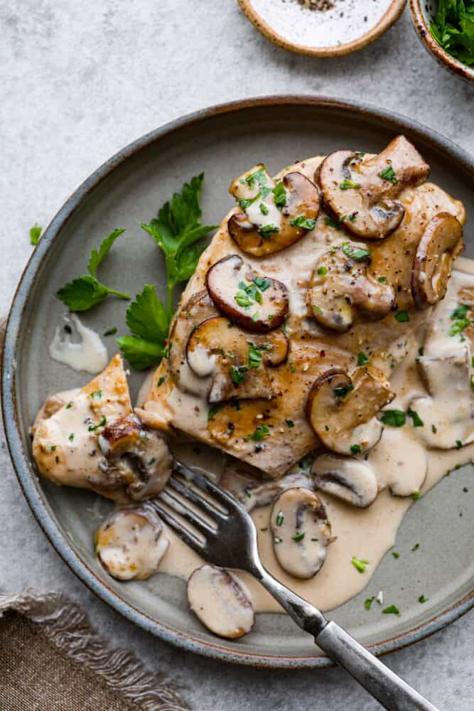Creamy Chicken Marsala is a classicย Italianย dish that is ready in under 30 minutes! Marsala wine is made into a creamy sauce paired with mushrooms for the ultimate savory bite. It's simple and easy to whip up and sure to be a crowd-pleaser! A piece of chicken on a plate with a fork taking a bite out of it.