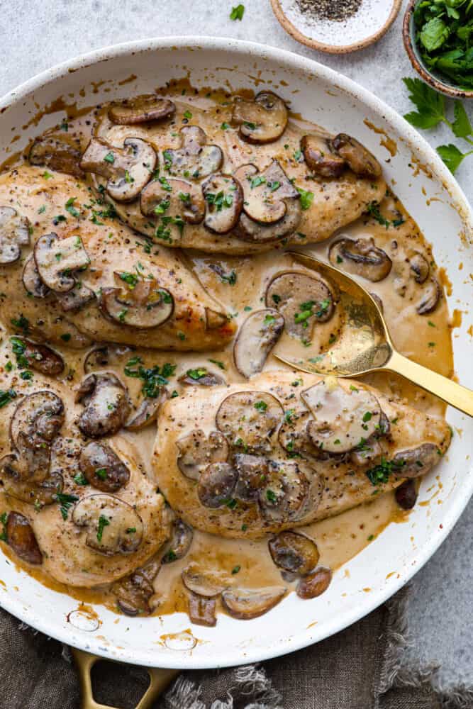 Creamy Chicken Marsala is a classicย Italianย dish that is ready in under 30 minutes! Marsala wine is made into a creamy sauce paired with mushrooms for the ultimate savory bite. It's simple and easy to whip up and sure to be a crowd-pleaser! Creamy chicken marsala on a plate with a golden spoon.