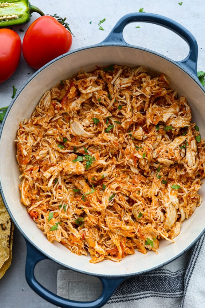 If you're a fan of Mexican cuisine, you have to try chicken tinga! This delicious dish is a classic from the Puebla region and is made with shredded chicken that's been simmered in a flavorful tomato-based sauce with smoky chipotle peppers. The result is a savory, slightly spicy, and oh-so-tasty dish that's perfect for tacos, tostadas, or just served over rice. Trust me, once you taste it, you'll be hooked! Chicken tinga in a white and blue skillet.