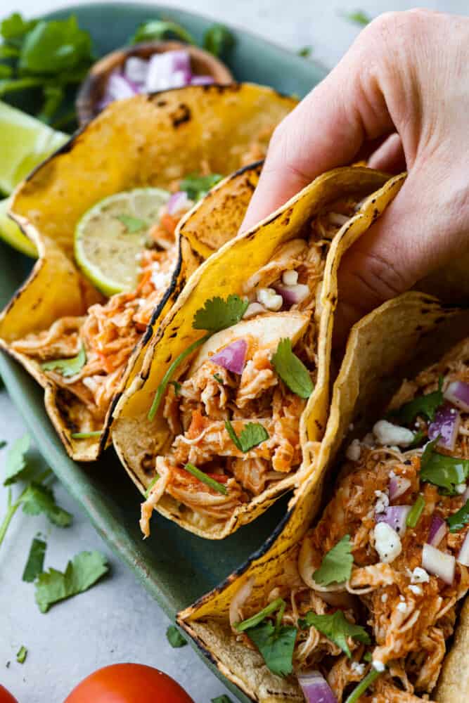 If you're a fan of Mexican cuisine, you have to try chicken tinga! This delicious dish is a classic from the Puebla region and is made with shredded chicken that's been simmered in a flavorful tomato-based sauce with smoky chipotle peppers. The result is a savory, slightly spicy, and oh-so-tasty dish that's perfect for tacos, tostadas, or just served over rice. Trust me, once you taste it, you'll be hooked! Closeup of a taco being picked up.