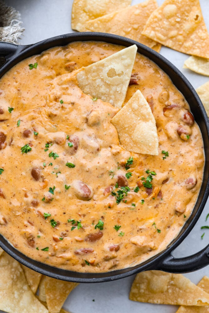 Time to break out the chips, because this homemade chili cheese dip is one appetizer you don’t want to miss! Hot, gooey, and oh-so-satisfying, this cheesy dip is guaranteed to make any gathering a hit. Top-down view of chili cheese dip served with chips in a black bowl.