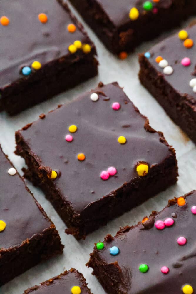 Brace yourself for a cosmic trip down memory lane! Homemade cosmic brownies are here to take you back to your childhood, one fudgy bite at a time. Because let's be real, there's no better way to relive the good old days than with a sprinkle-studded treat that's out of this world! Closeup of Cosmic Brownies, cut into squares.