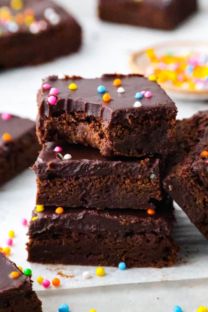 Brace yourself for a cosmic trip down memory lane! Homemade cosmic brownies are here to take you back to your childhood, one fudgy bite at a time. Because let's be real, there's no better way to relive the good old days than with a sprinkle-studded treat that's out of this world! 3 brownies stacked on top of each other. One has a bite taken out of it.