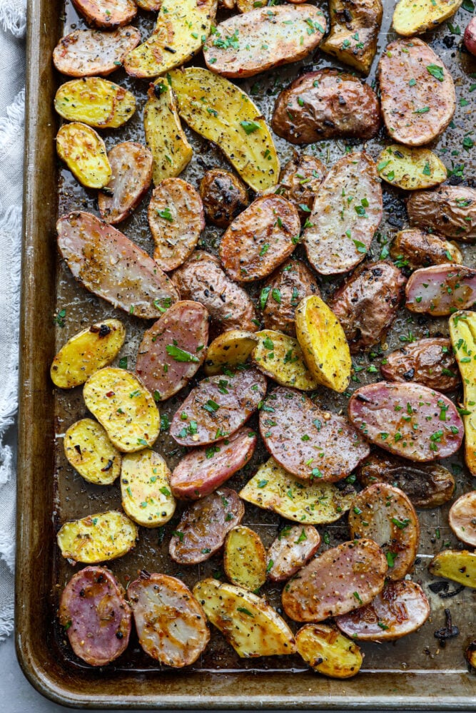 Roasted Fingerling Potatoes are thin skinned and crispy on the outside, yet so creamy and smooth on the inside. They are smaller potatoes, so they cook quickly and are loaded with fresh seasonings that make these potatoes irresistible. Fingerling potatoes on a baking sheet.