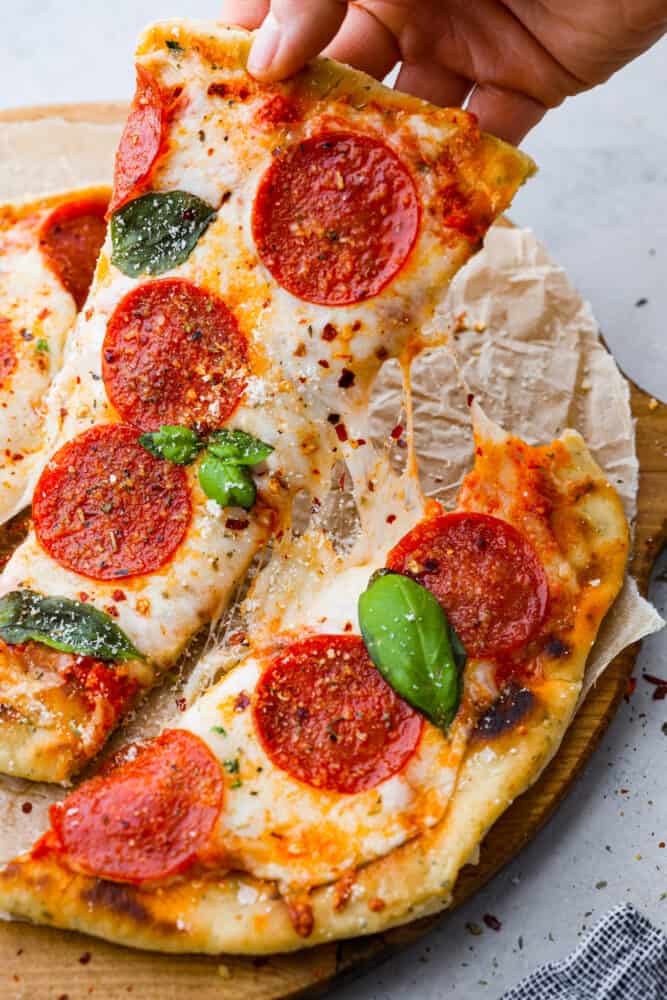 Flatbread pizza is a simple and delicious recipe that is easier to make than regular pizza. With a thin and chewy flatbread crust that is topped with your favorite pizza toppings, it's even better than takeout and always a hit! A hand picking up a piece of pizza.